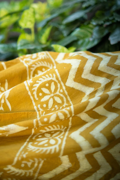 Yellow fabric with white patterns against a green leafy background