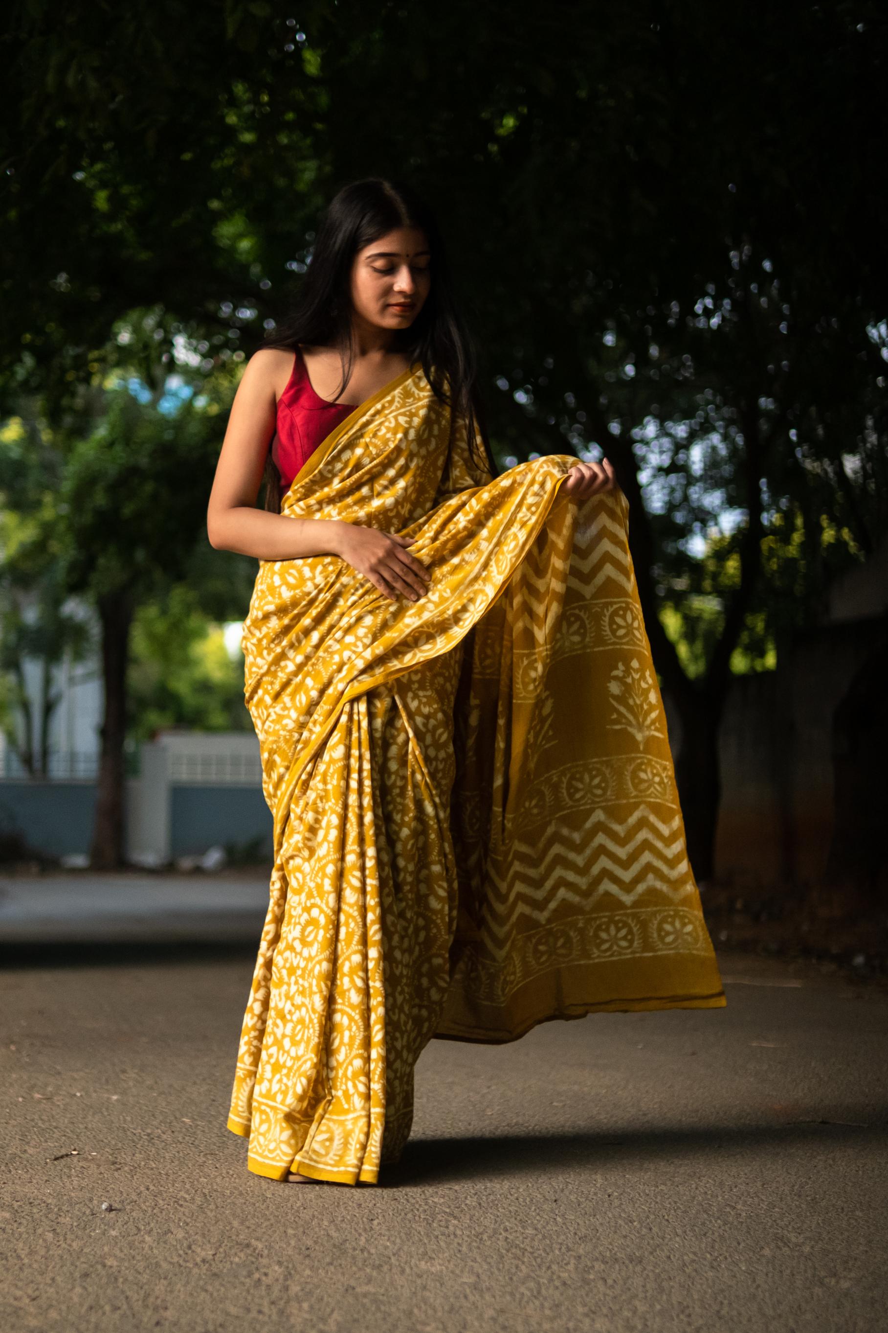 Woman in a yellow saree with a red blouse standing outdoors.
