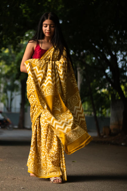 Woman in a yellow saree with a red blouse standing outdoors.