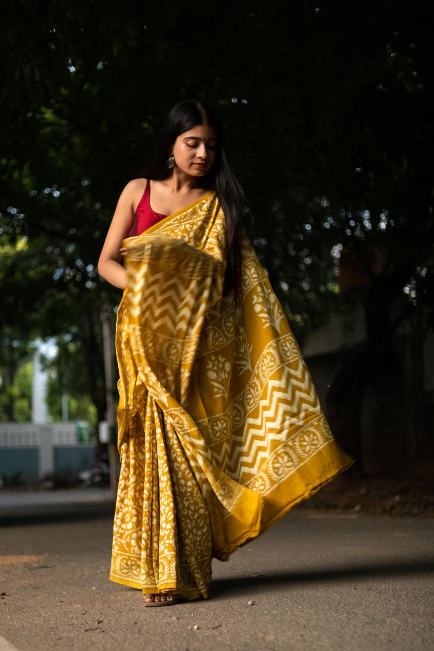 Woman in a yellow saree with a red blouse walking outdoors.