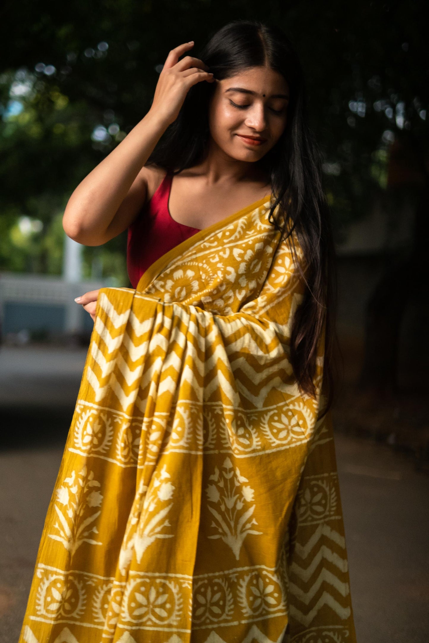 Woman holding a yellow patterned saree with a blurred outdoor background