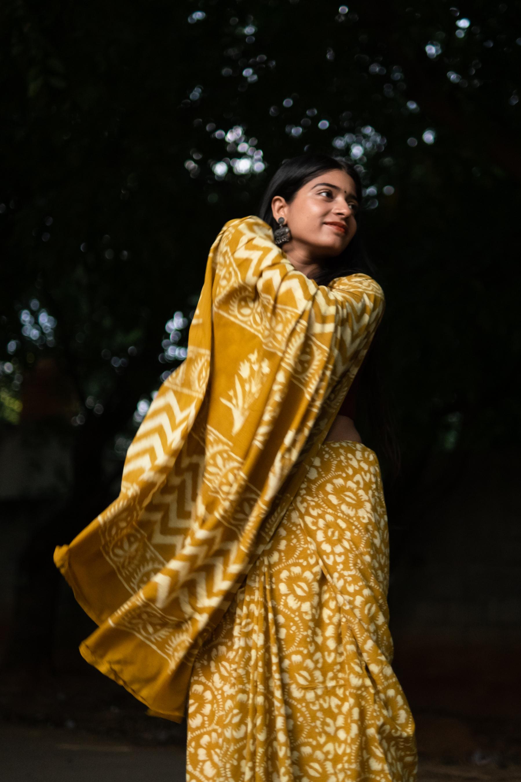 Woman wearing a yellow patterned saree against a dark background