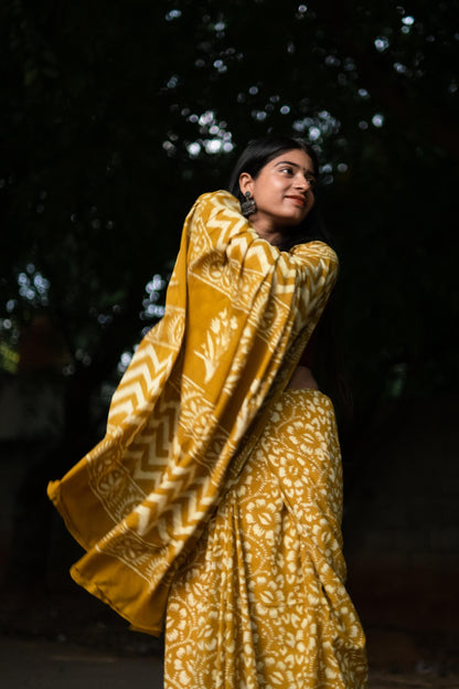 Woman wearing a yellow patterned saree against a dark background